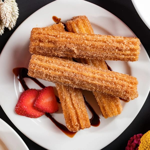 Mezcal Express Dearborn churros, sugar-dusted and drizzled with chocolate, served with fresh strawberries.