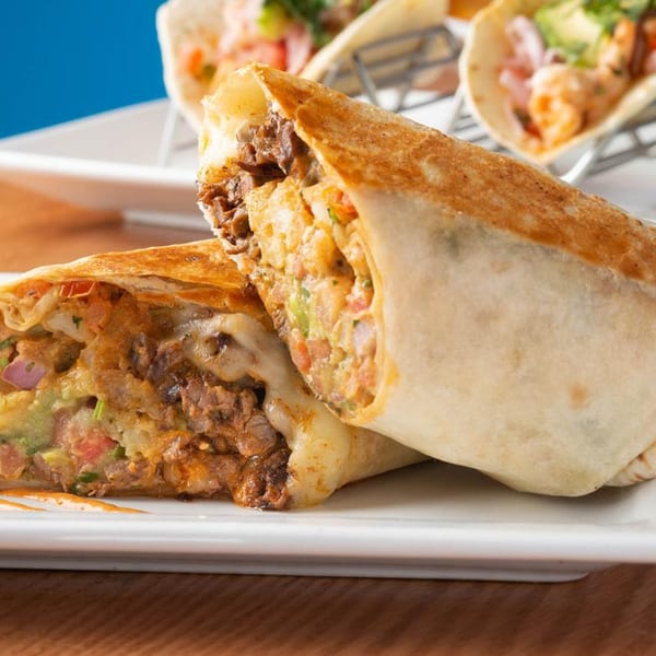A large, sliced burrito filled with meat, cheese, and vegetables on a white plate.